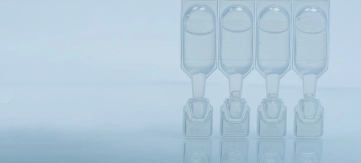 four clear plastic ampoules with liquid arranged in a row on light background